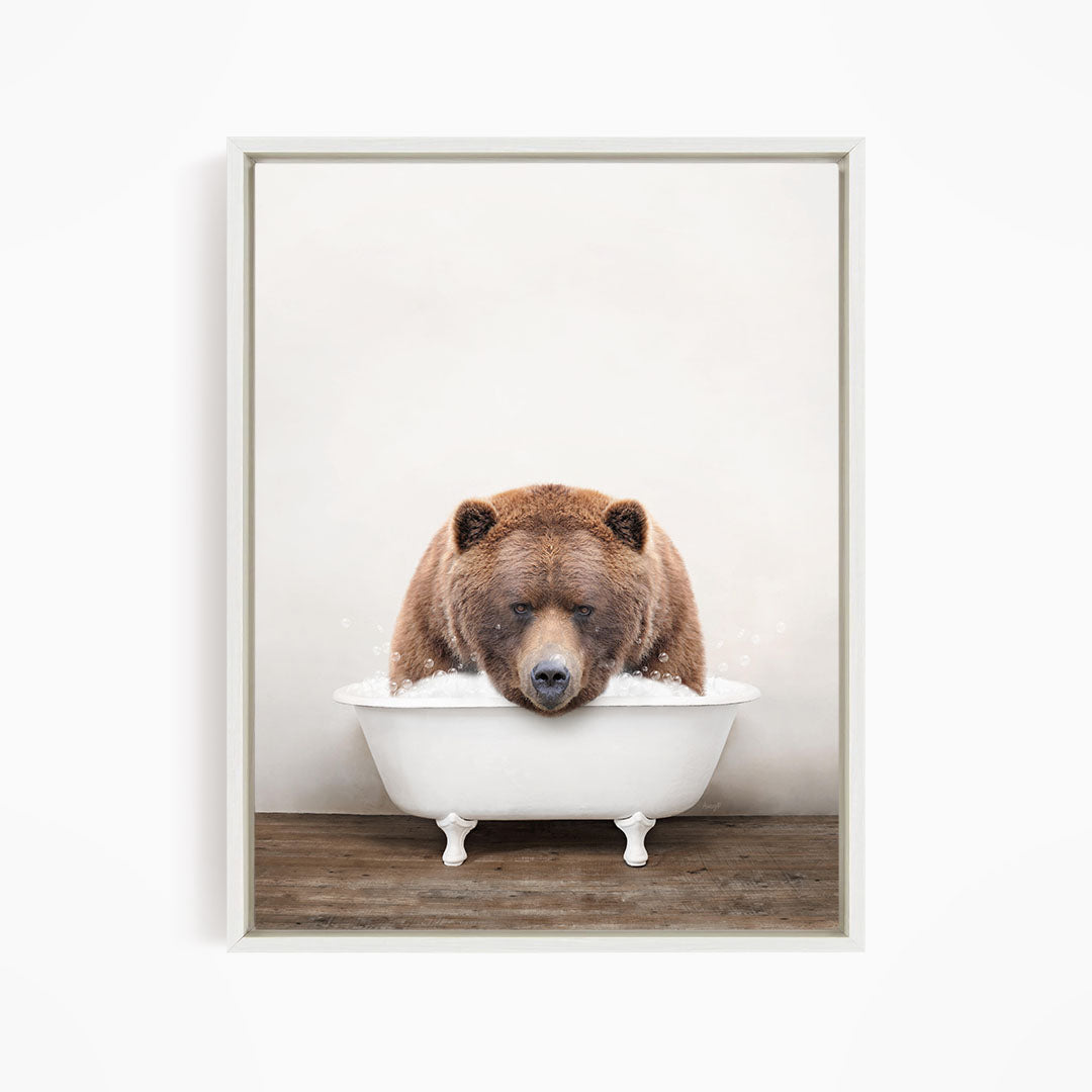 A brown bear sitting in a white bathtub filled with water, appearing to enjoy the bath.