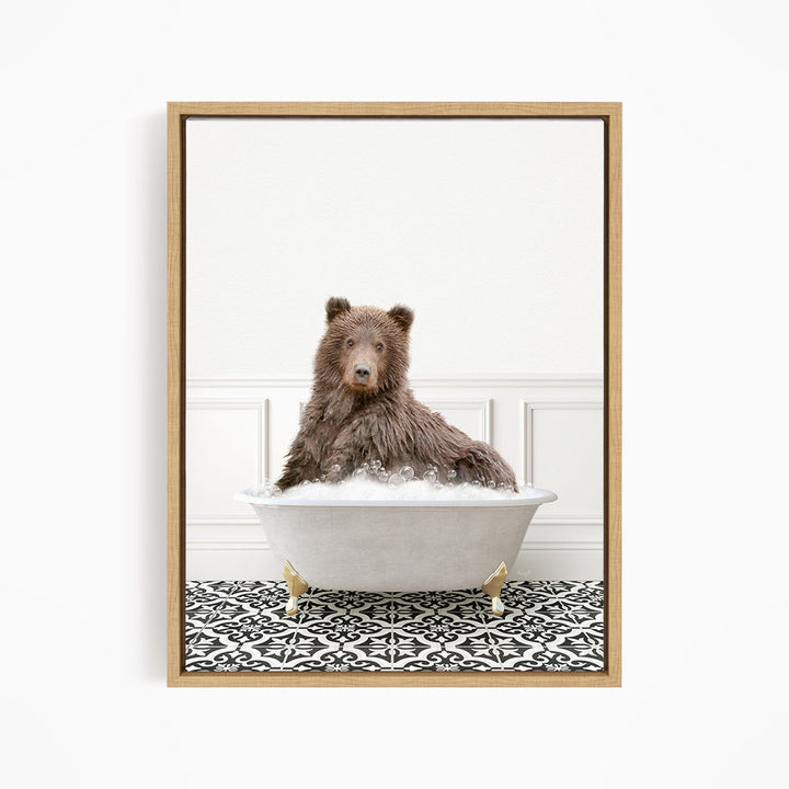 A brown bear sitting in a white bathtub filled with bubbles, looking directly at the camera.