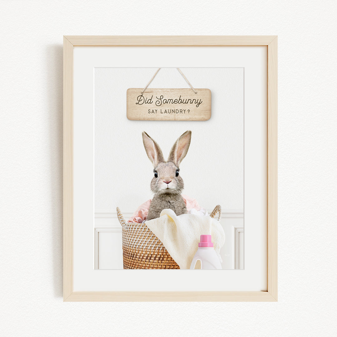 A framed image of a rabbit sitting in a basket filled with laundry, with a sign above it that says "Did Somebunny Say Laundry".