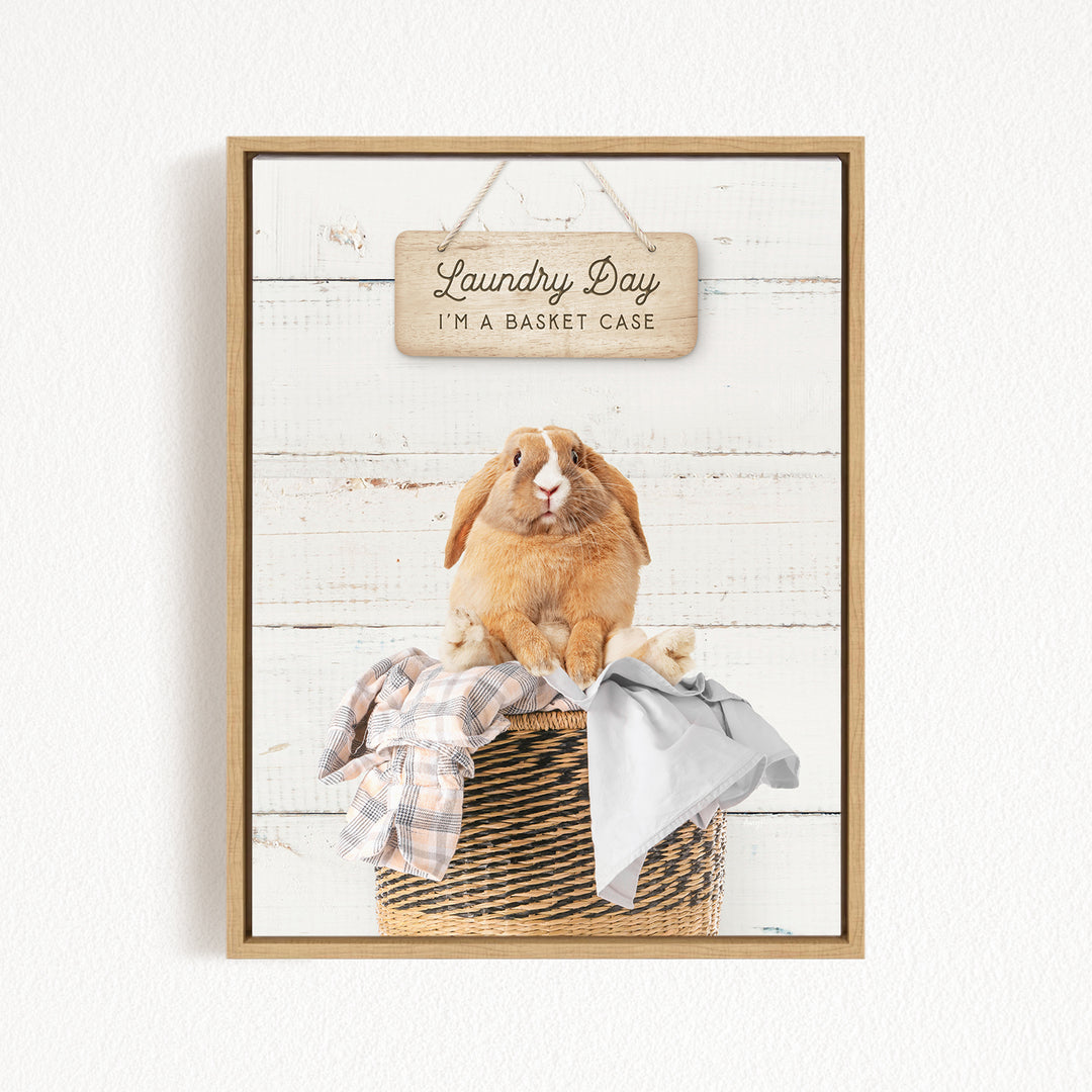A wooden sign with the text "Laundry Day I'm a basket case" hangs above a basket containing clothes and a small rabbit.