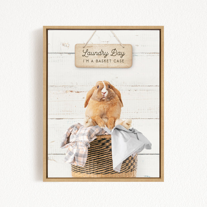 A wooden sign with the text "Laundry Day I'm a basket case" hangs above a basket containing clothes and a small rabbit.