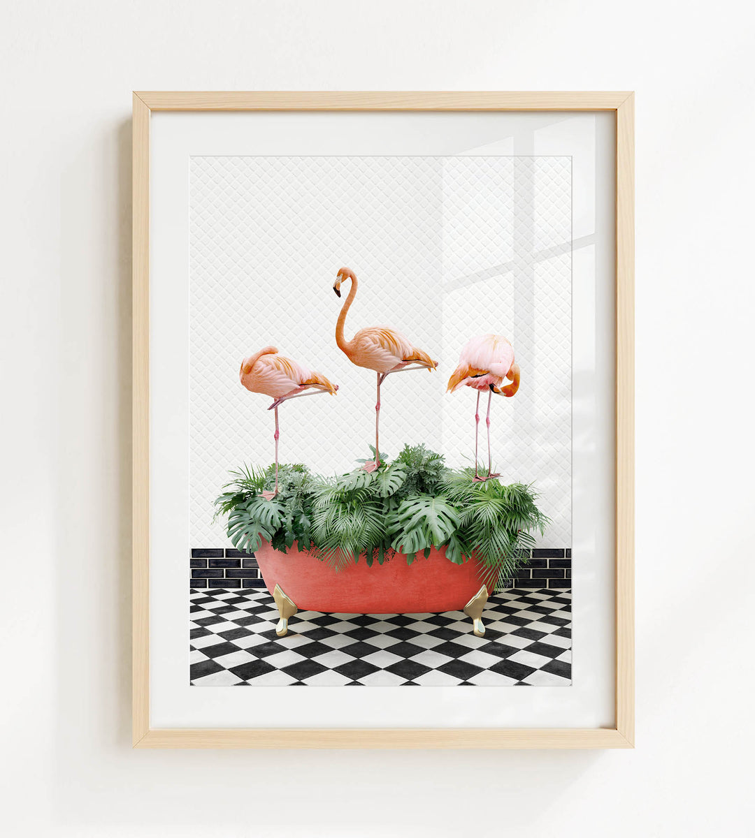 A framed image of three flamingos standing on a black and white checkered floor, with a red planter filled with greenery in the foreground.