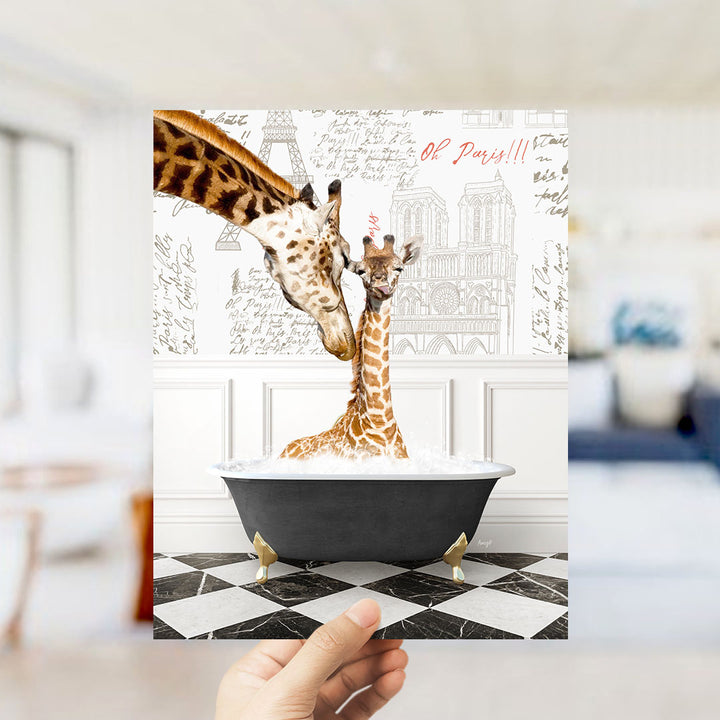 A hand holds up a framed image depicting two giraffes in a bathtub, with a Paris-themed background.