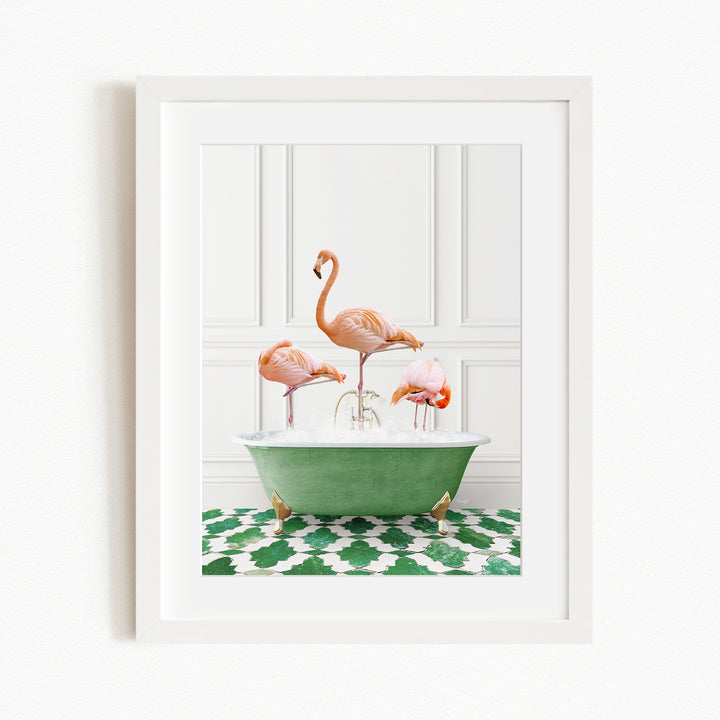 A framed image depicting three pink flamingos standing in a green bathtub on a patterned green and white rug.