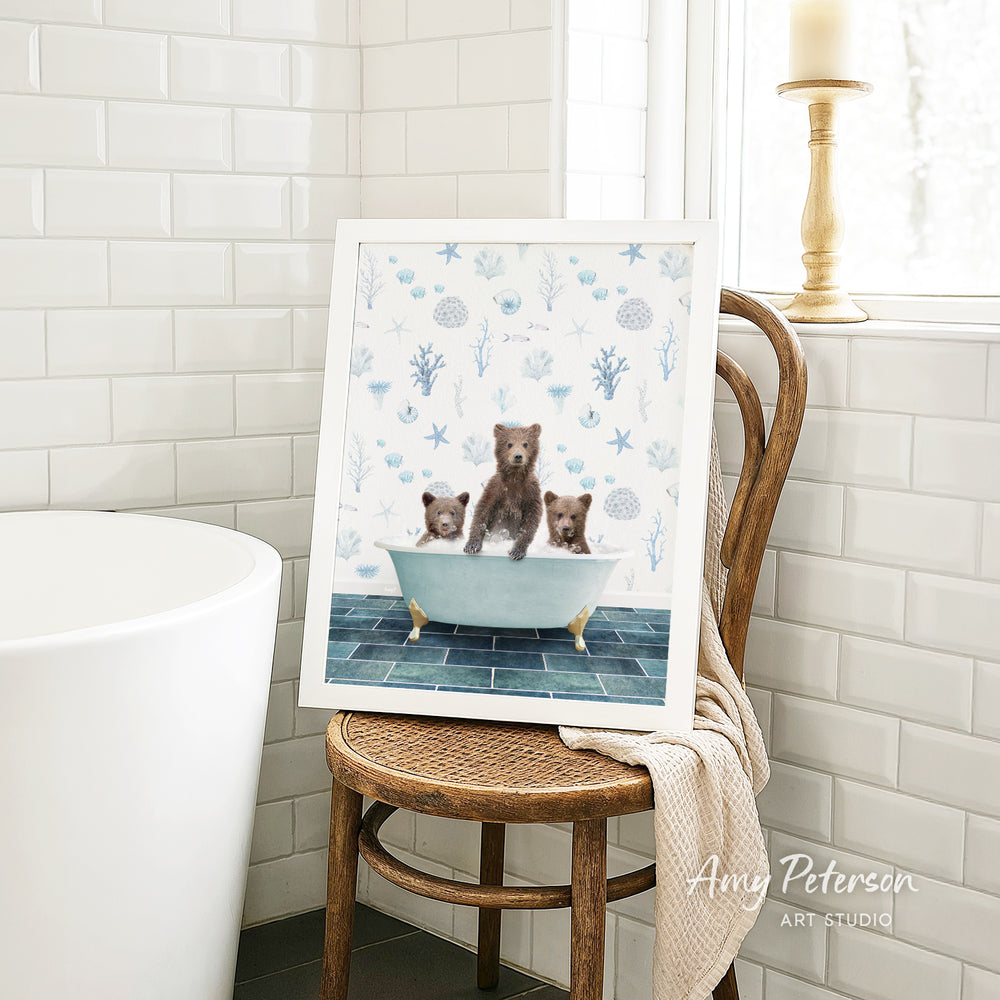 A framed painting of three bears sitting in a bathtub is displayed on a wooden chair in a bathroom.