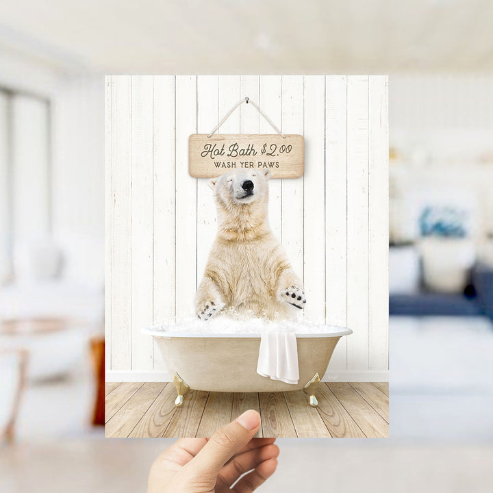 A hand holding a framed image of a polar bear sitting in a bathtub, with a sign above it that says "Hot Bath $2.00 WASH YER PAWS".