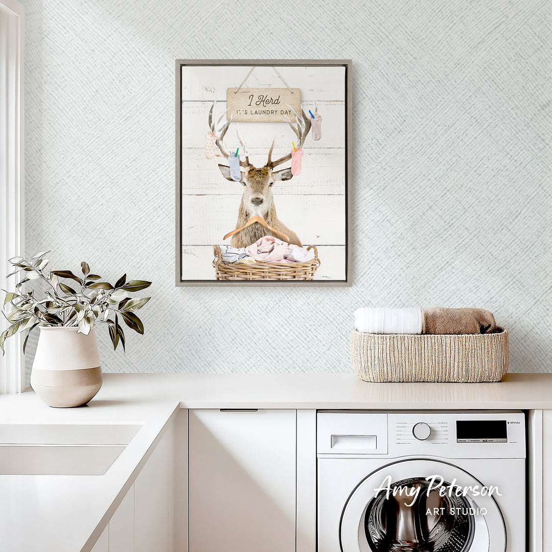 a framed picture of a deer with antlers, sitting in a basket, hanging on a wall above a white countertop with a plant and a basket of towels.