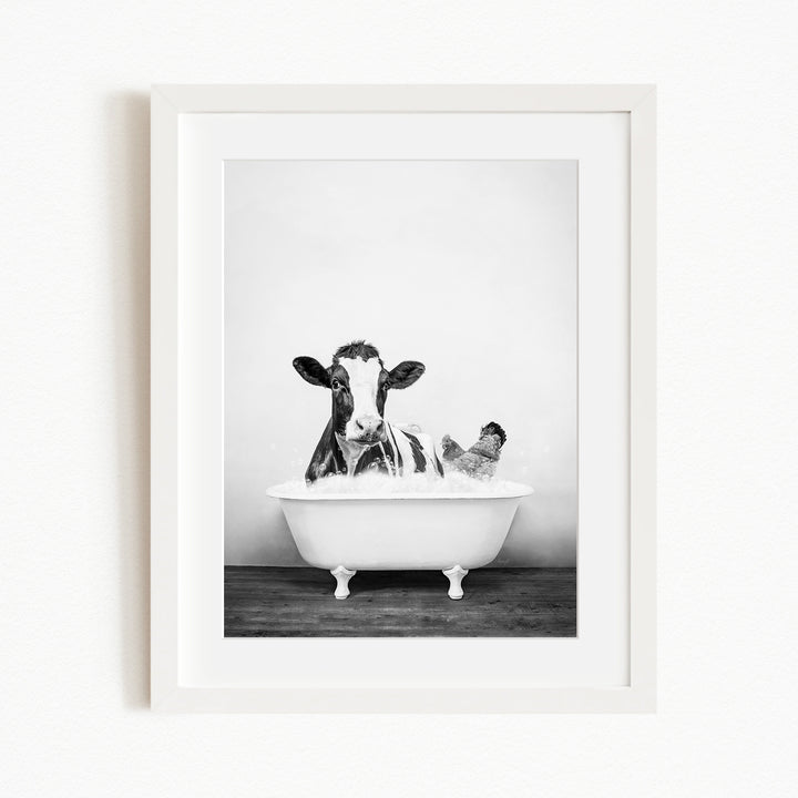 A black and white image of a cow sitting in a bathtub, with a person sitting next to it.