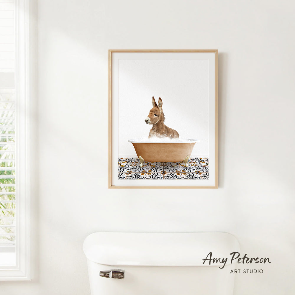 A framed print of a donkey sitting in a bathtub is hanging on a white wall.