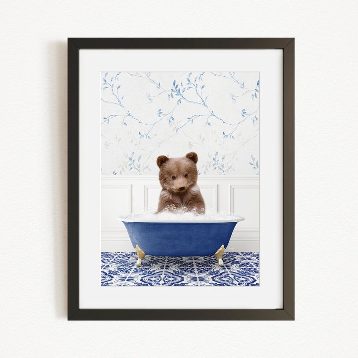A small brown bear is sitting in a blue bathtub filled with water, surrounded by a blue and white patterned rug on the floor.