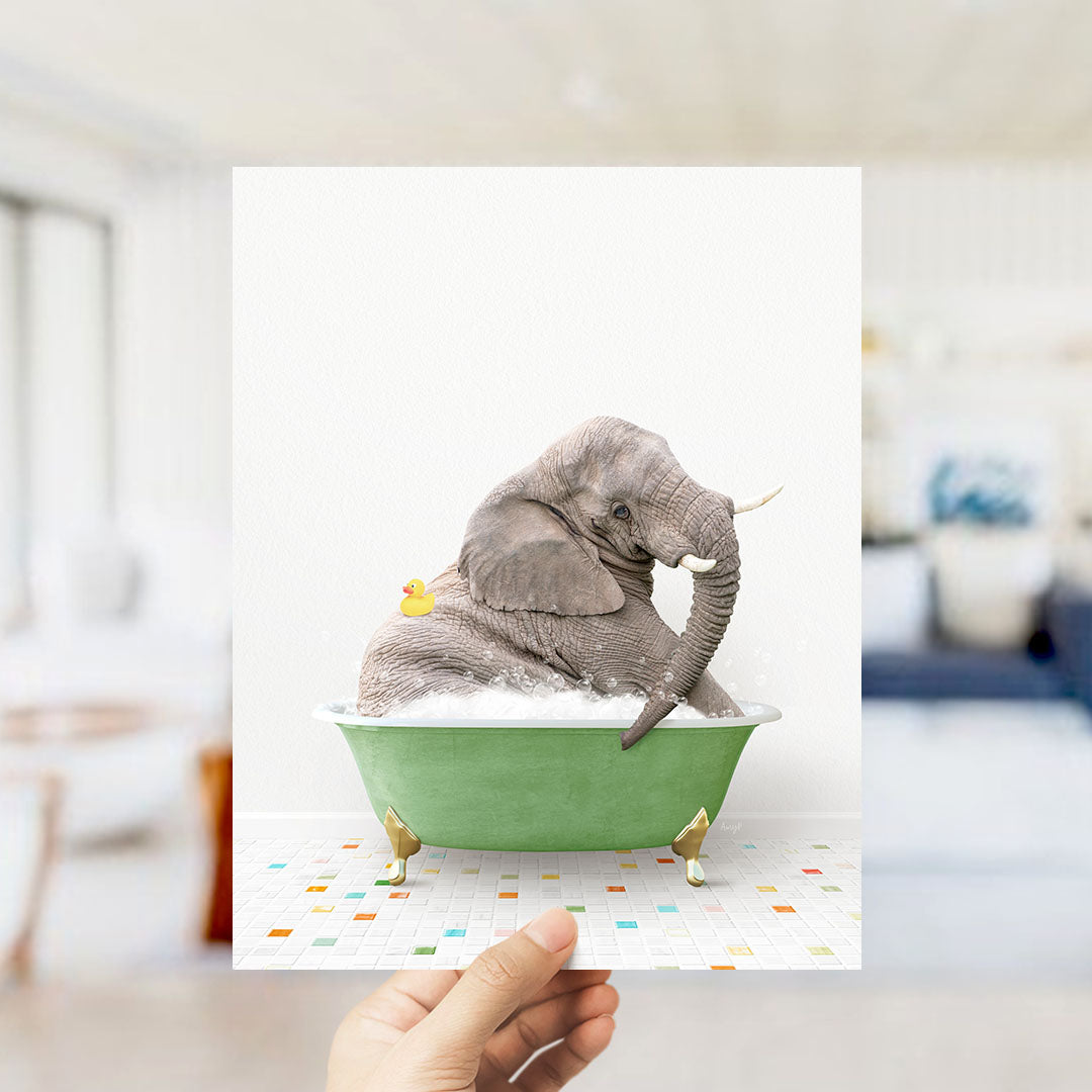 A hand holds up a framed image of a gray elephant sitting in a green bathtub, with a yellow rubber duck floating nearby.