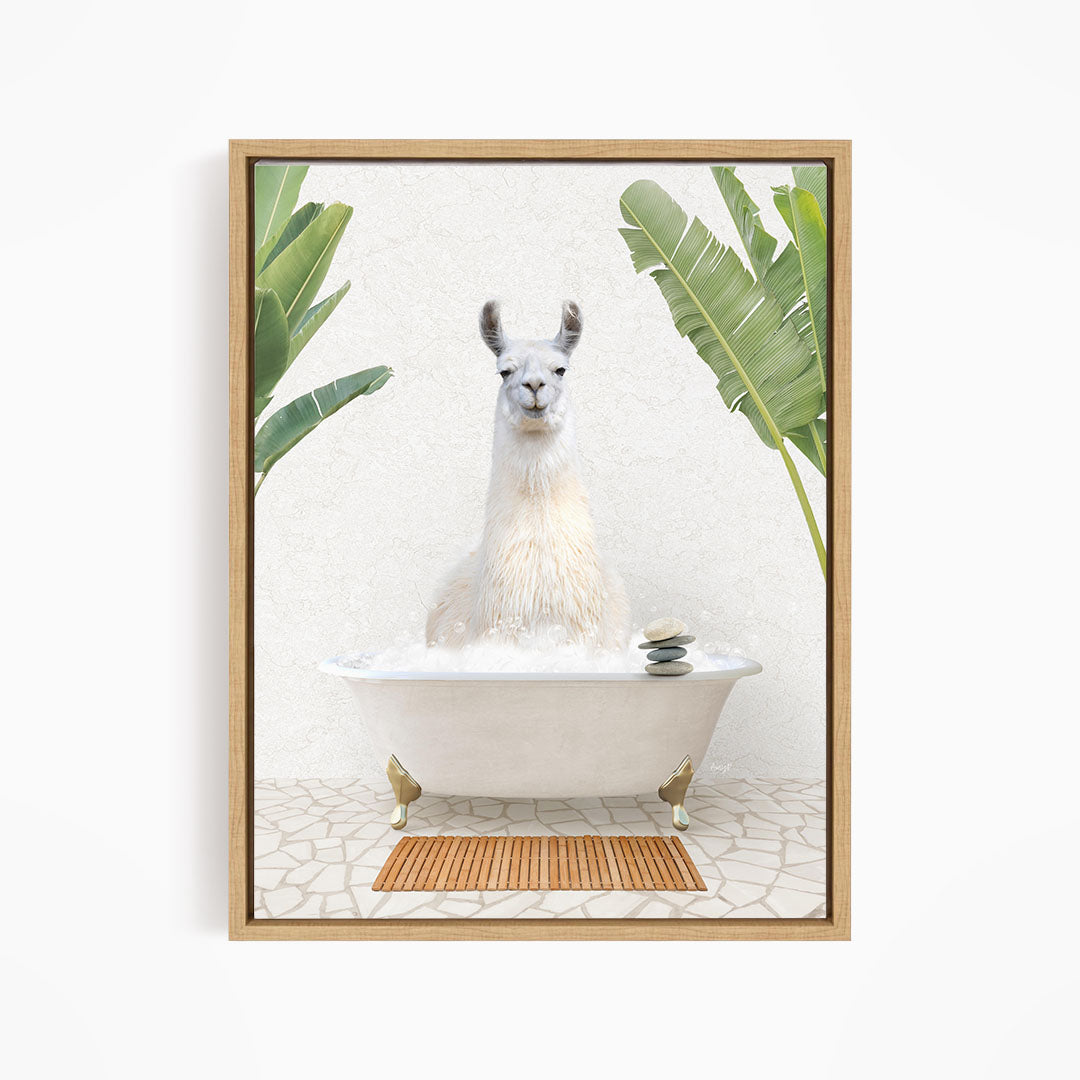 A white llama sitting in a white bathtub filled with bubbles, surrounded by green leaves and a wooden mat on the floor.