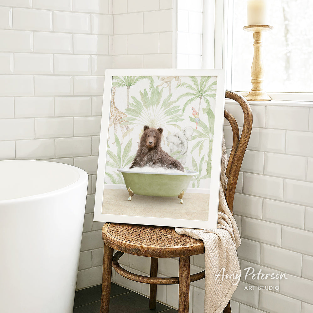 A framed image of a brown bear sitting in a green bathtub, surrounded by tropical foliage, is displayed on a wooden chair in a bathroom setting.