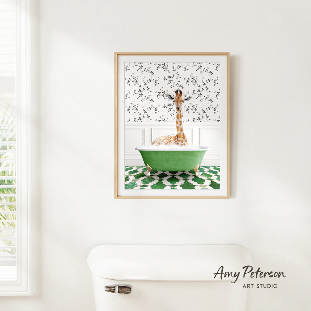 A framed print of a giraffe sitting in a green bathtub is hanging on a white wall in a bathroom.