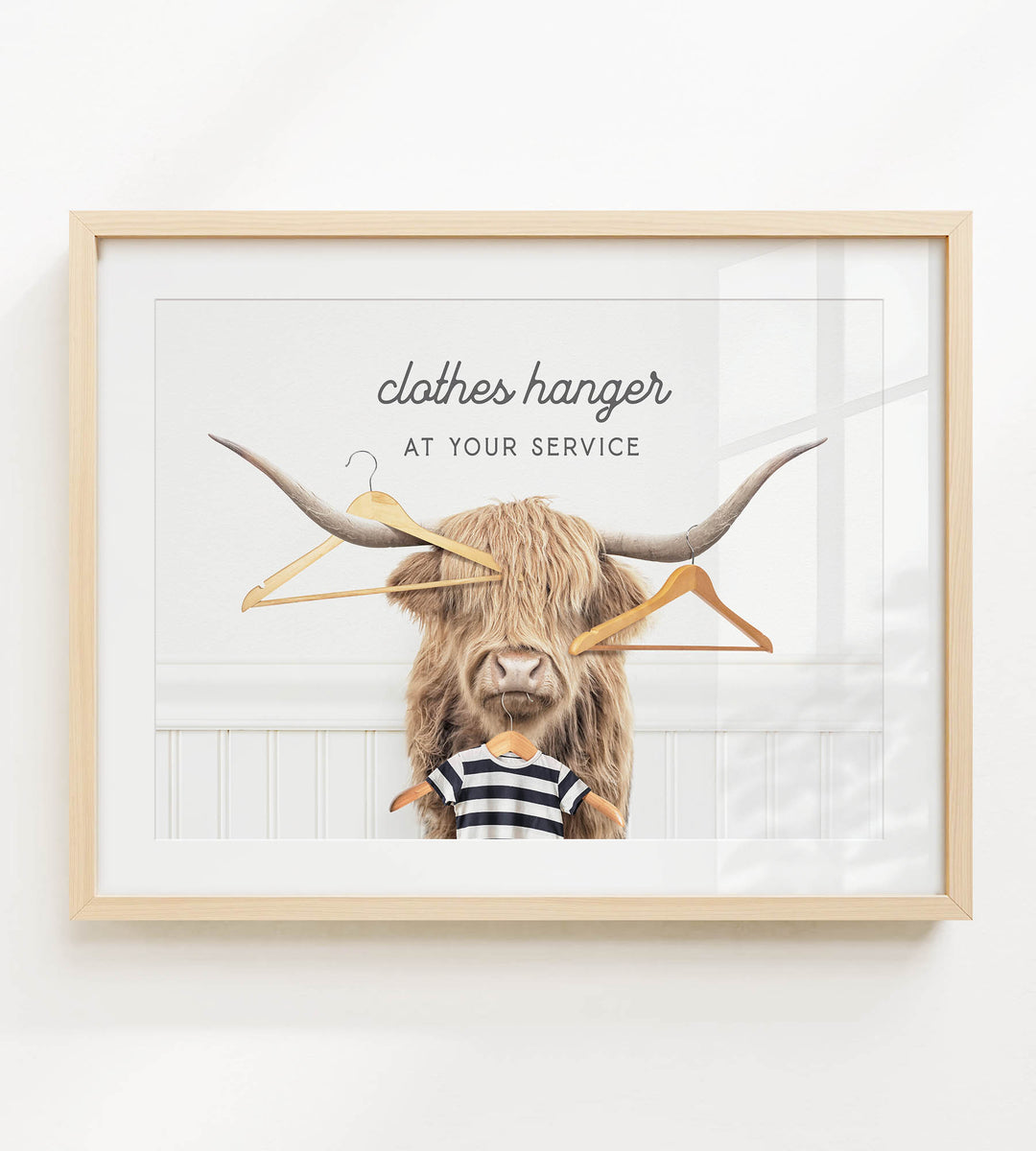 A framed image depicting a large, furry animal with long horns, wearing a striped shirt and surrounded by hanging clothes hangers.