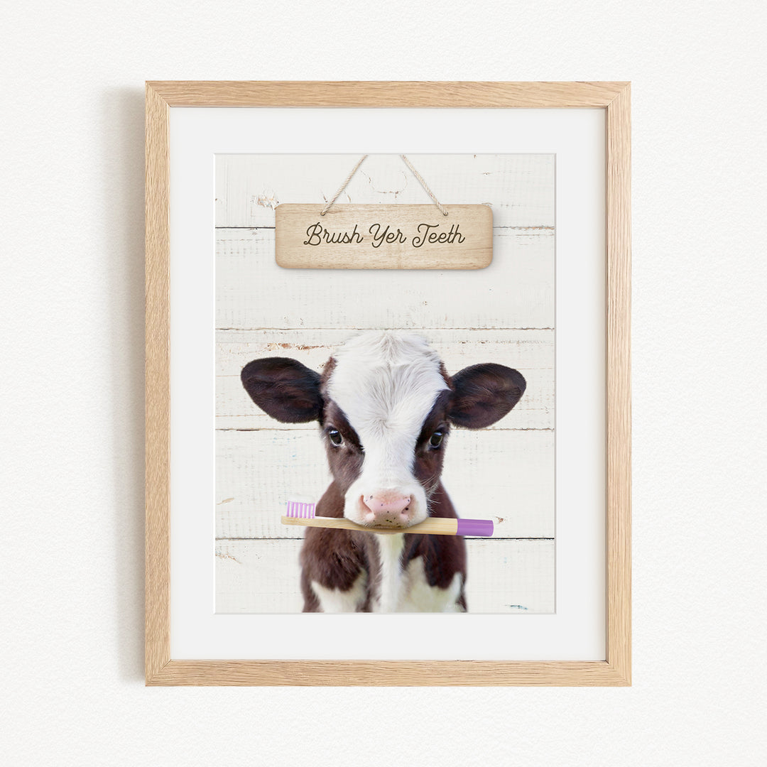 A framed image of a cow holding a toothbrush in its mouth, with a wooden sign above it that says "Brush Your Teeth".