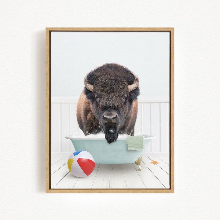 A buffalo with large horns is sitting in a bathtub filled with water, surrounded by a beach ball, towel, and starfish.