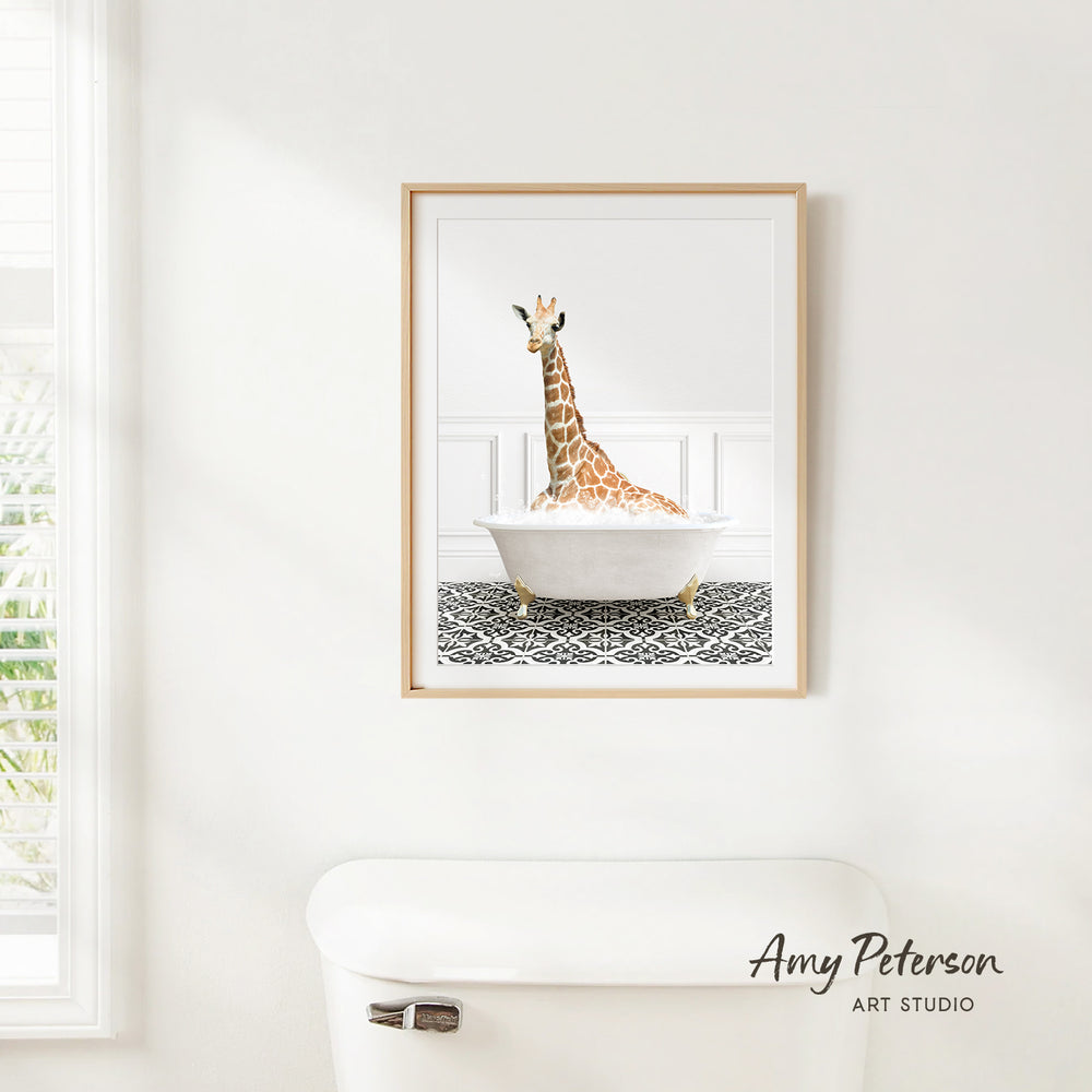 A framed print of a giraffe sitting in a bathtub is hanging on a white wall.