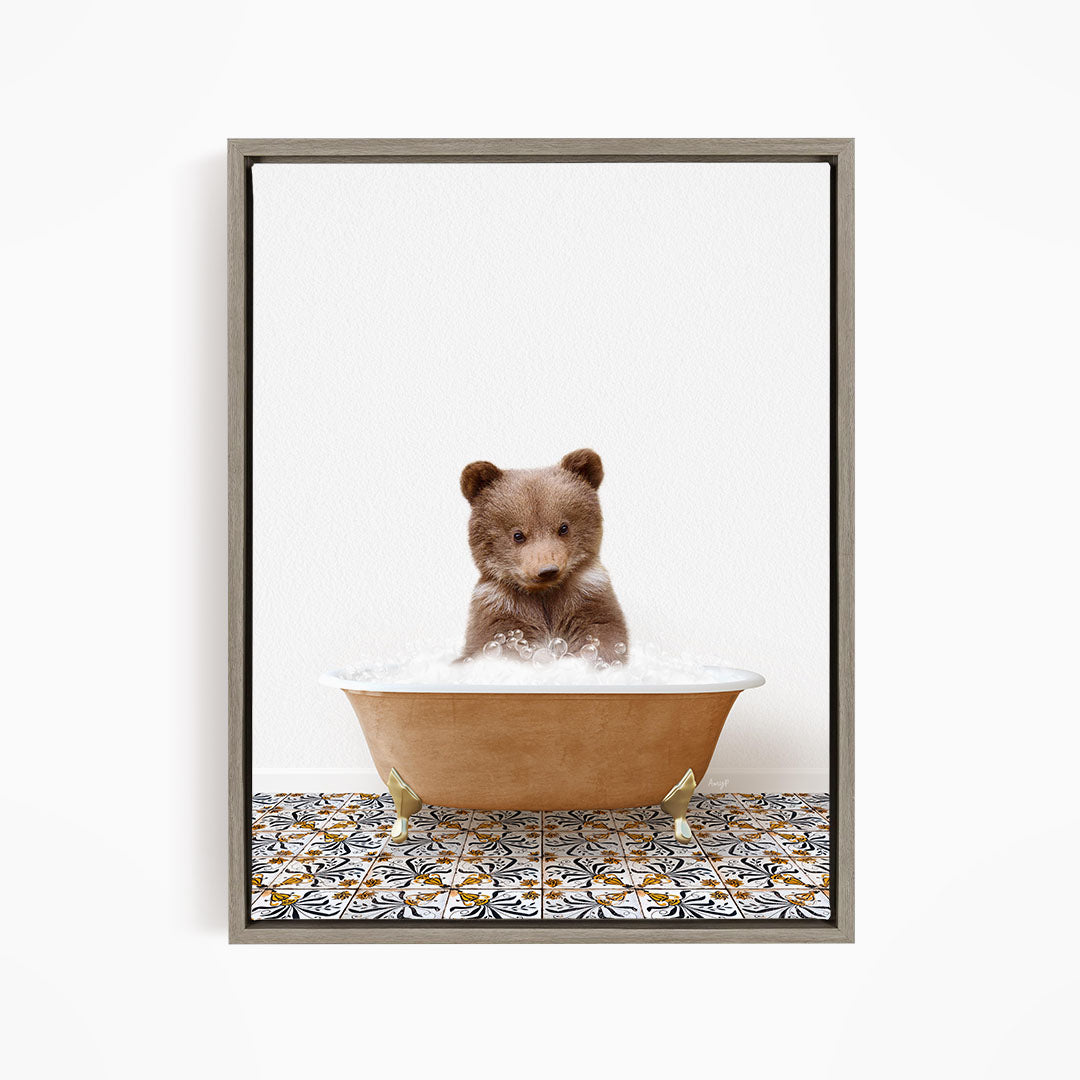 A cute brown bear cub sitting in a bathtub filled with bubbles, looking directly at the camera.