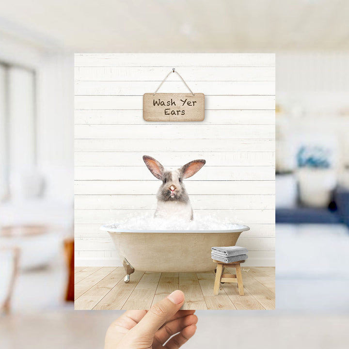 A hand holding a picture of a rabbit sitting in a bathtub, with a sign above that says "Wash Your Ears".