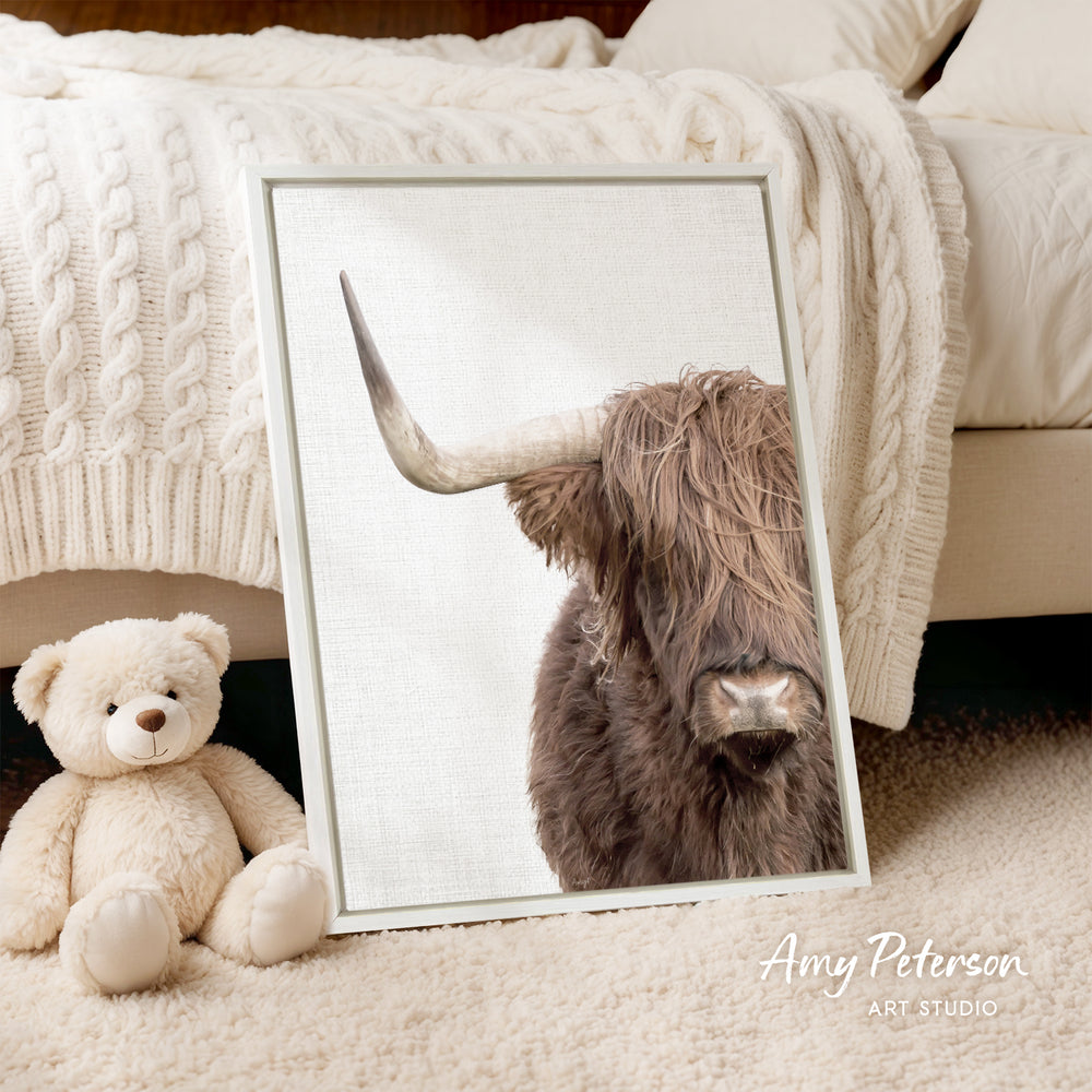 A framed image of a horned animal, likely a yak or a yak dog, is displayed on a white bedspread. Next to the framed image is a stuffed teddy bear.