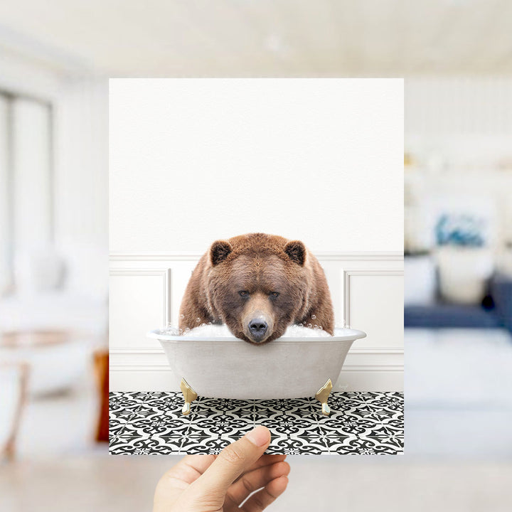 A brown bear sitting in a white bathtub filled with water, with a hand holding the image up to the camera.