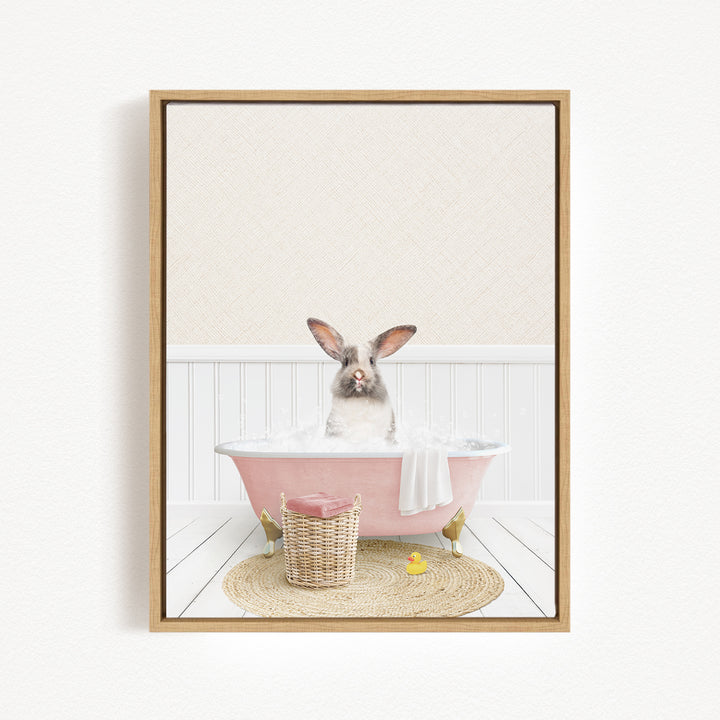 A rabbit sitting in a pink bathtub filled with bubbles, surrounded by a basket of toys and a yellow rubber duck.