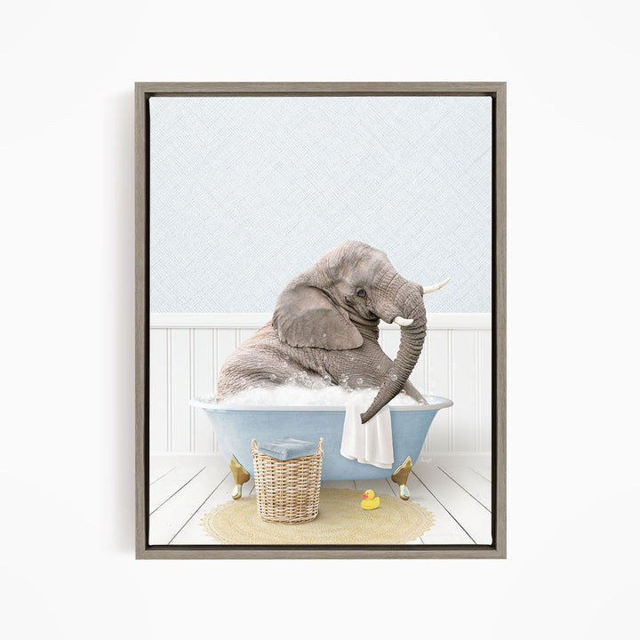 A gray elephant is sitting in a blue bathtub filled with water, surrounded by a yellow rubber duck and a basket.