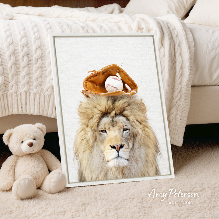 A framed print of a lion wearing a baseball glove on its head, with a teddy bear next to it, is displayed on a bed.