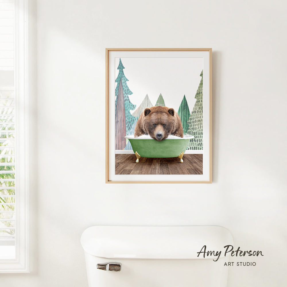 A framed print of a brown bear sitting in a green bathtub, surrounded by pine trees, is hanging on a white wall.