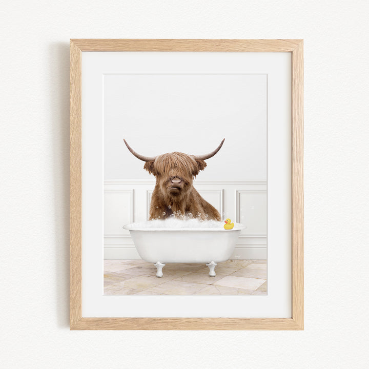 A brown Highland cow with large horns is sitting in a white bathtub filled with water, with a yellow rubber duck floating in the tub.