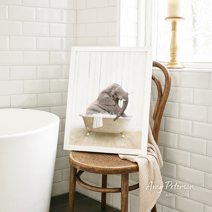 A framed image of a gray elephant sitting in a bathtub, with a towel draped over the side of the tub.