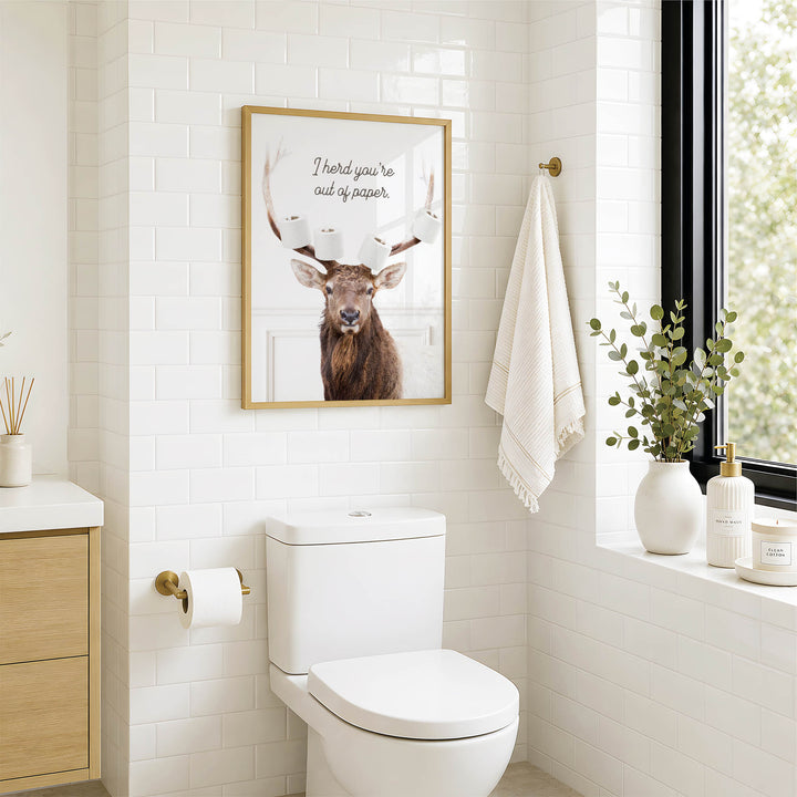 A bathroom with a white toilet, a framed picture of a deer with antlers, and a towel hanging on a rack.