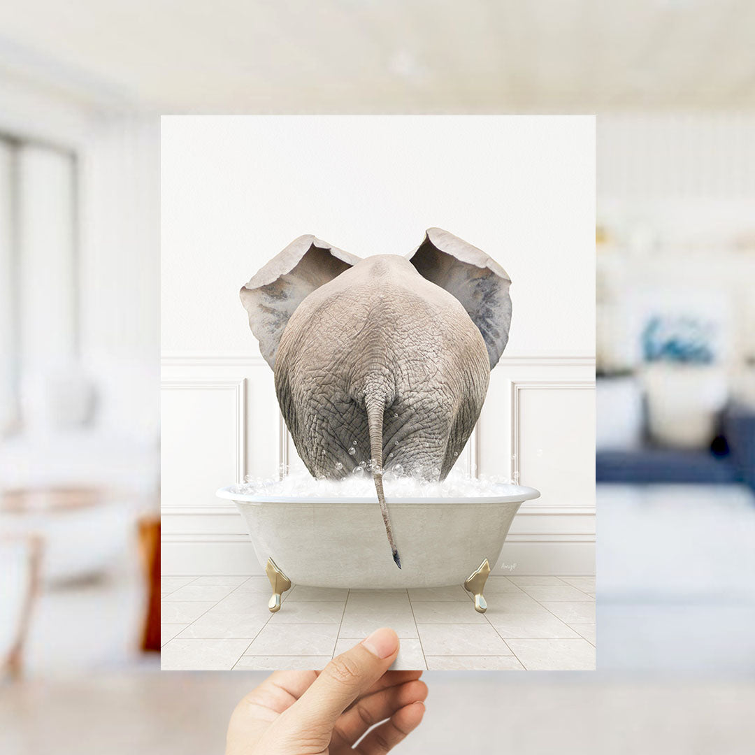 A hand holds up a framed image of an elephant sitting in a bathtub filled with water, creating a whimsical and playful scene.