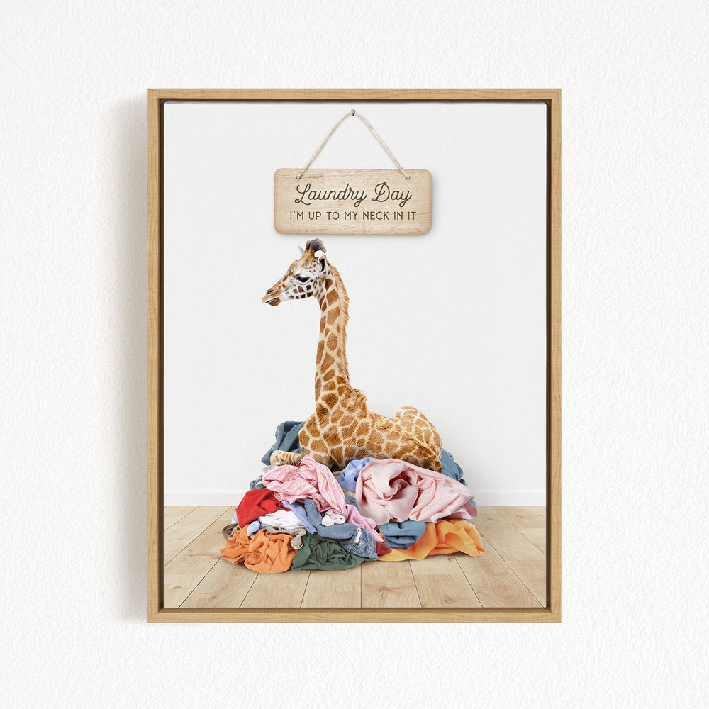 A giraffe standing on a pile of clothes, with a wooden sign above it that says "Laundry Day I'm up to my neck in it".