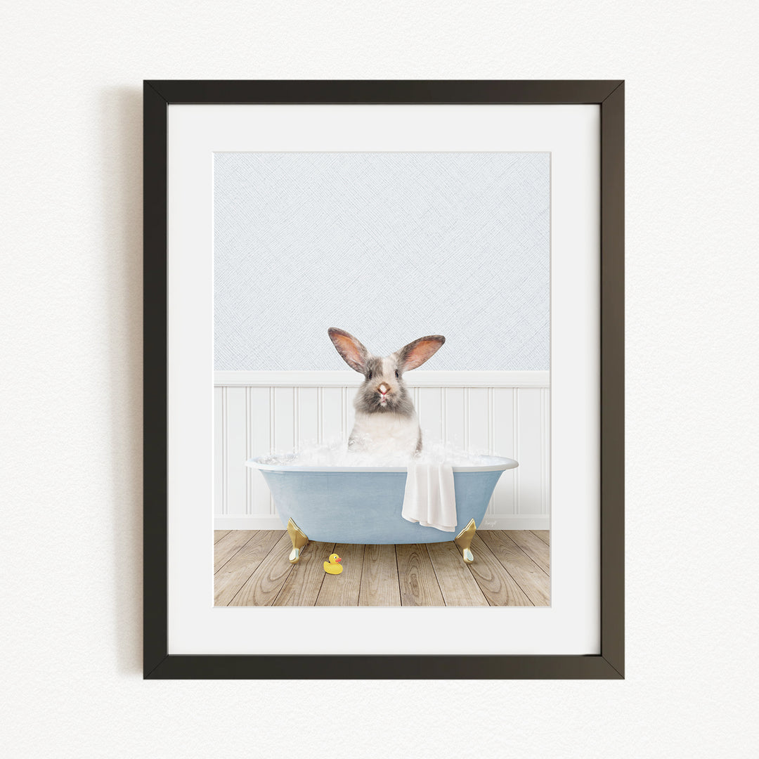 A white rabbit sitting in a blue bathtub filled with bubbles, with yellow rubber duckies floating around it.