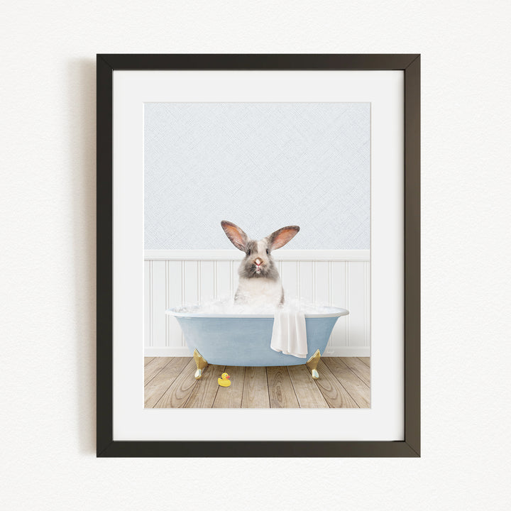 A white rabbit sitting in a blue bathtub filled with bubbles, with yellow rubber duckies floating around it.