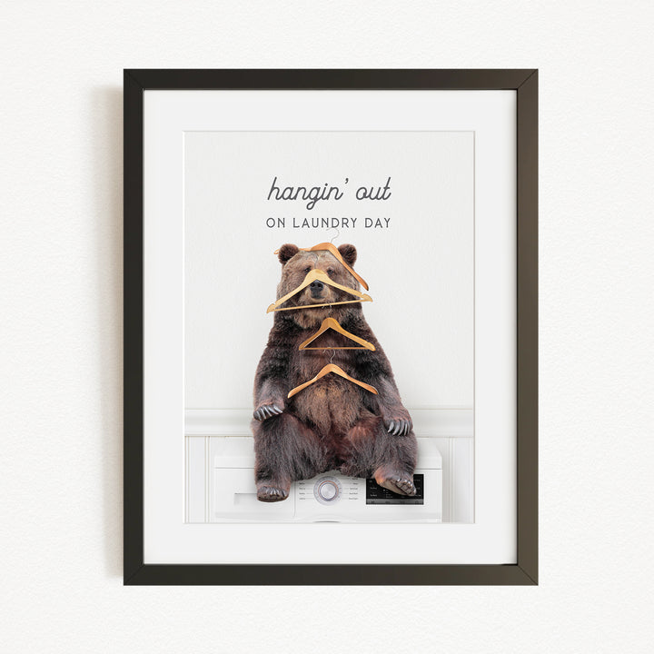 A framed image of a bear sitting on a washing machine, with the text "hangin' out on laundry day" written above it.