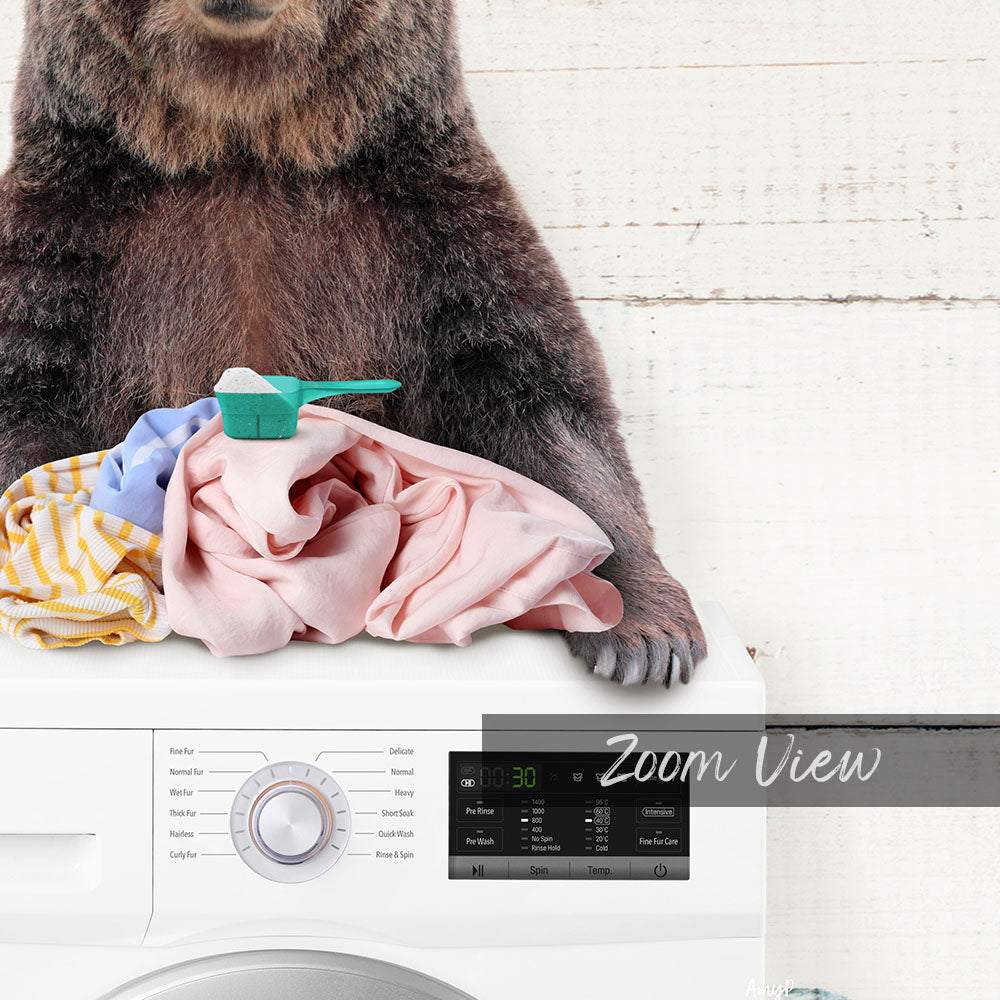 A bear sitting on top of a washing machine, surrounded by laundry.