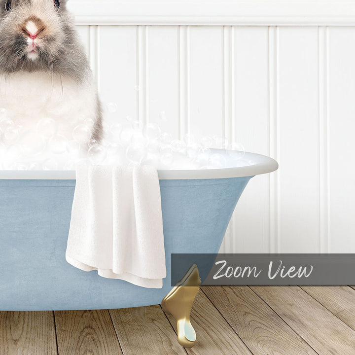 A fluffy gray and white rabbit sitting in a blue bathtub filled with bubbles, with a towel draped over the side and a "Zoom View" label below the image.