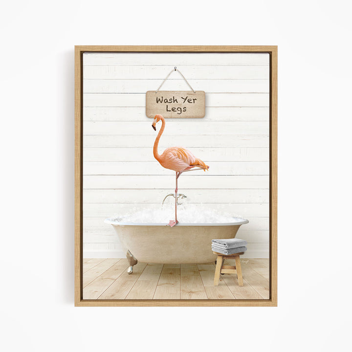 A framed image depicting a pink flamingo standing in a bathtub, with a sign above it that says "Wash Your Legs".