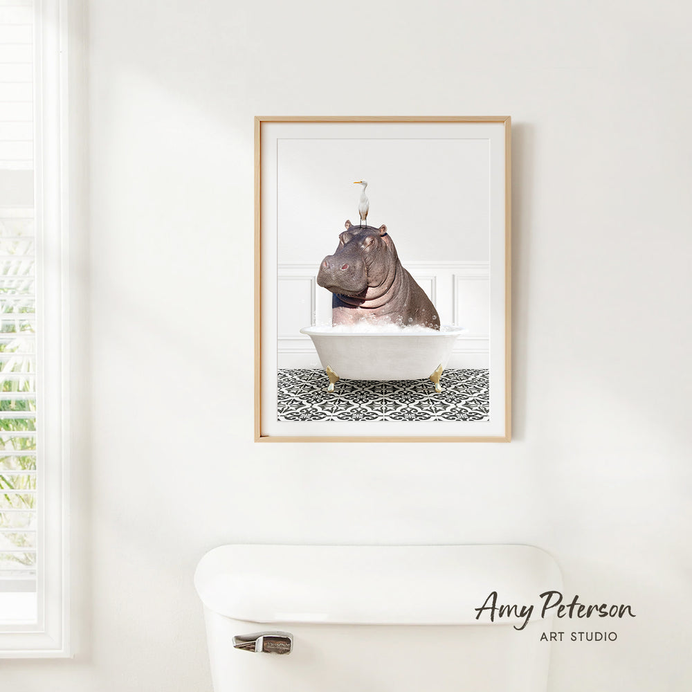 A framed image of a hippopotamus sitting in a bathtub is hanging on a white wall.