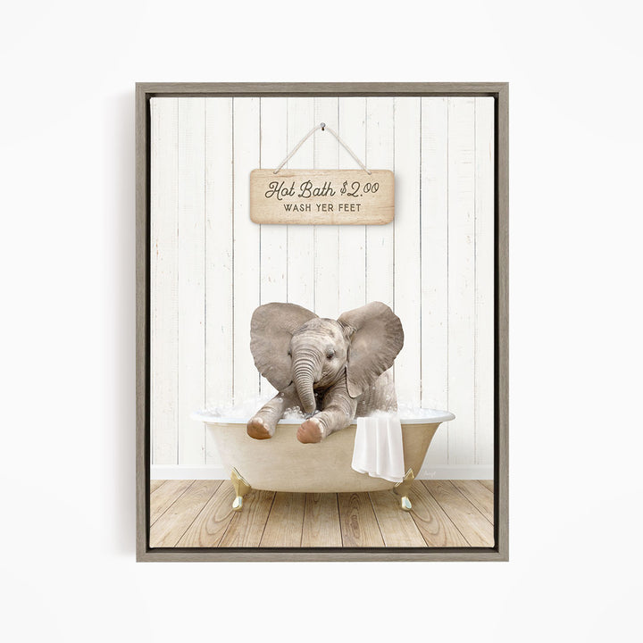 A wooden sign with the text "Hot Bath $2.00 WASH YOUR FEET" hangs on a white wooden wall, with a baby elephant sitting in a bathtub filled with water.
