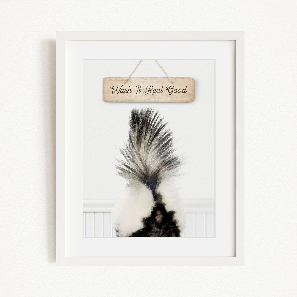 A framed image of a skunk's tail with the text "Wish It Real Good" written on a wooden sign above it.