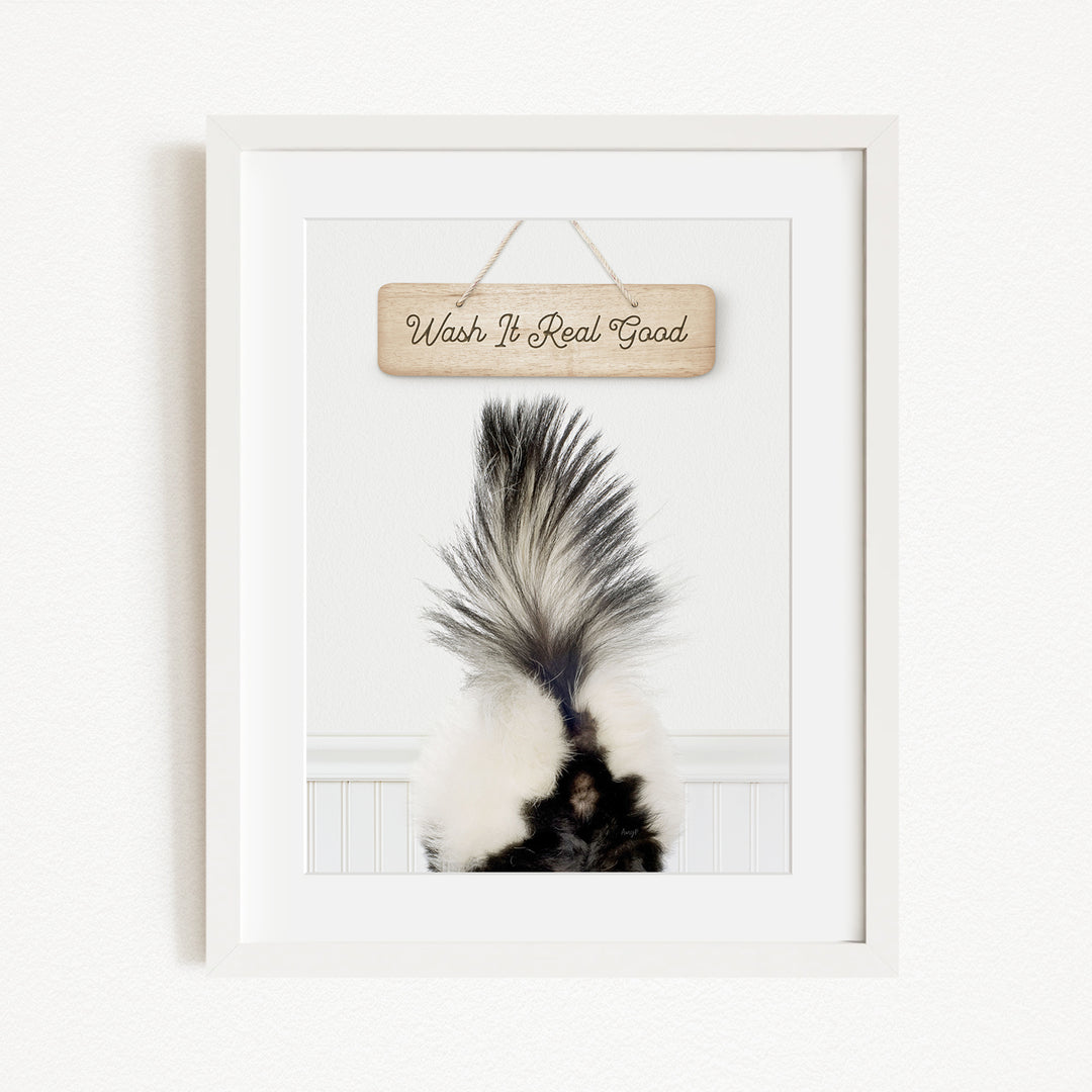 A framed image of a skunk's tail with the text "Wish It Real Good" written on a wooden sign above it.