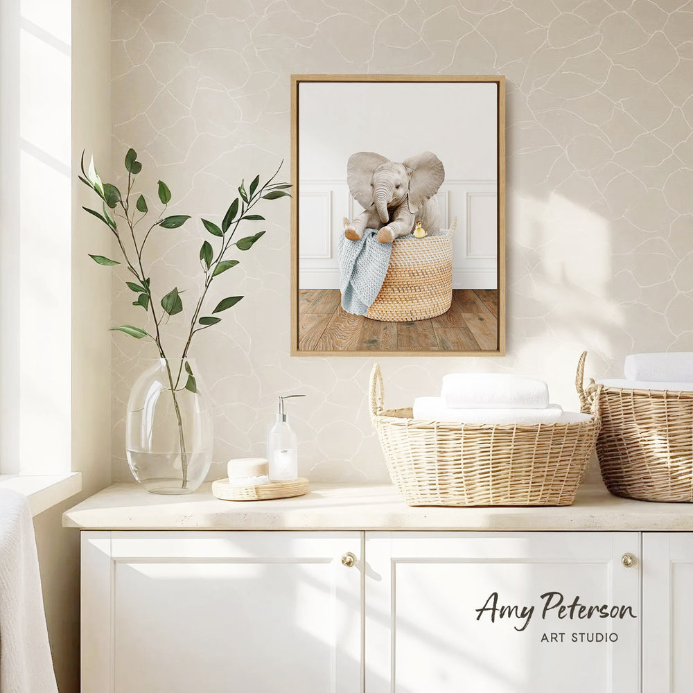 a cozy and well-decorated bathroom with a framed picture of an elephant sitting in a basket, a vase with green leaves, and baskets on a counter.