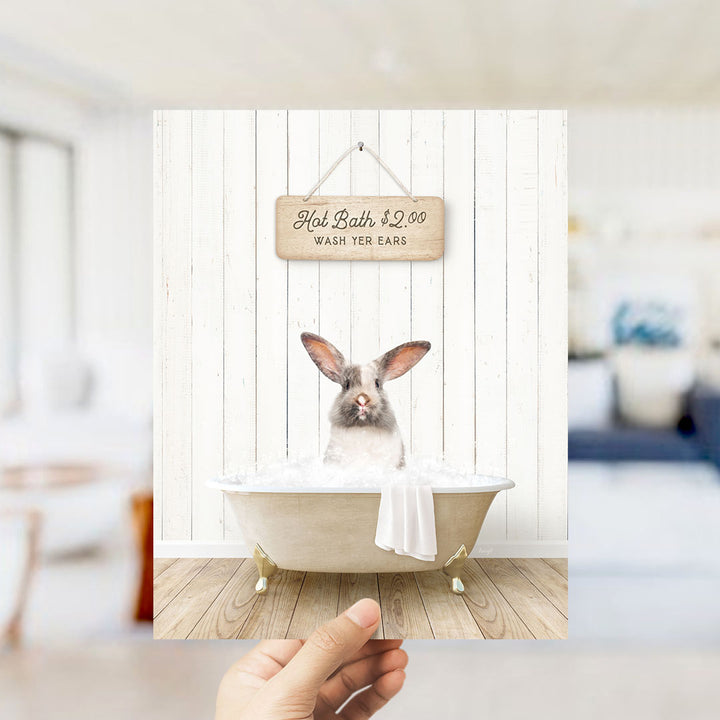 A hand holding a framed image of a rabbit sitting in a bathtub, with a sign above it that says "Hot Bath $2.00 WASH YOUR EARS".