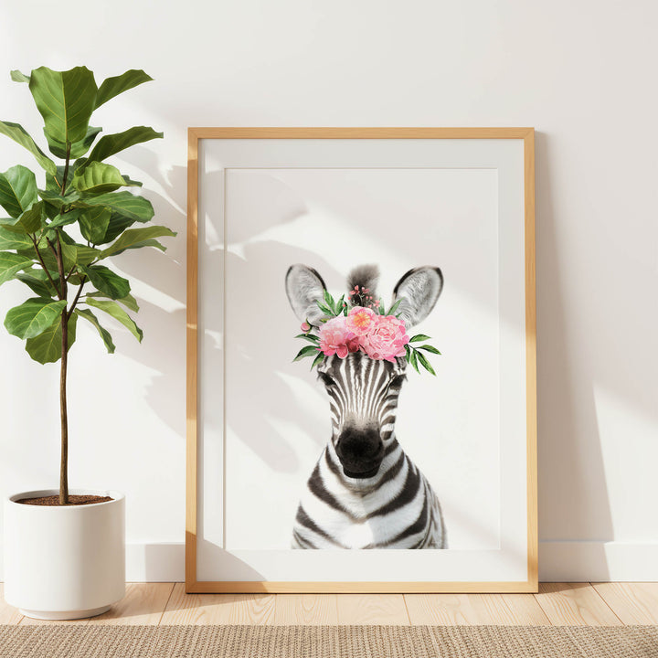 A framed print of a zebra with a floral headpiece is displayed on a white wall, accompanied by a potted plant to the left.