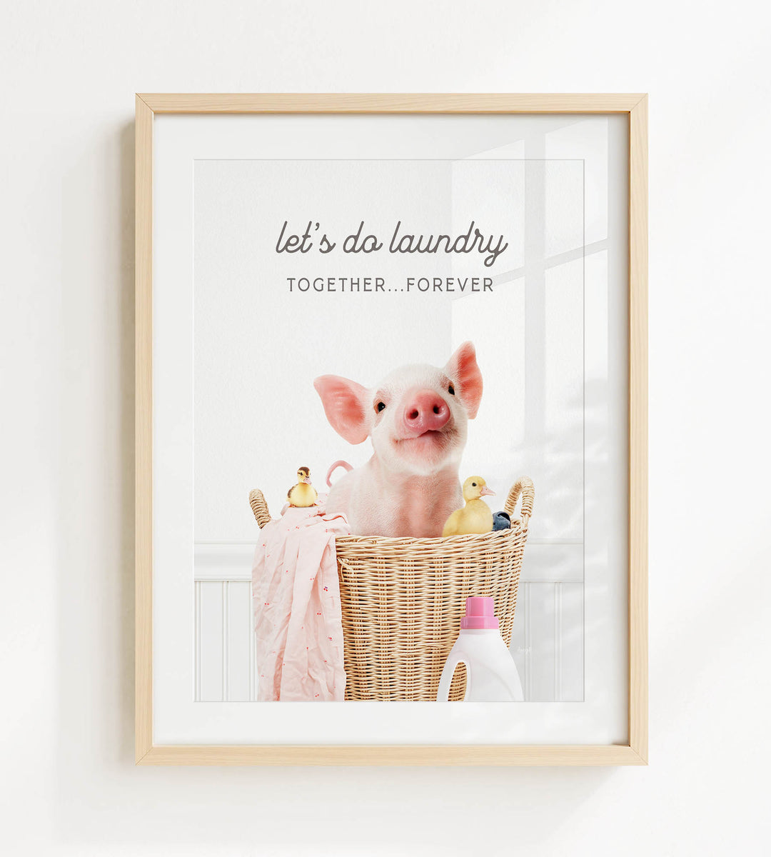 A framed image of a pig sitting in a wicker basket filled with various objects, including a bottle of detergent and a yellow rubber duck.