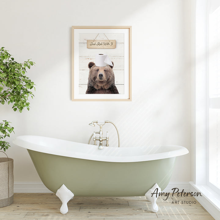 a bathroom with a green clawfoot bathtub, a framed picture of a bear wearing a toilet paper hat, and a potted plant on the left side.